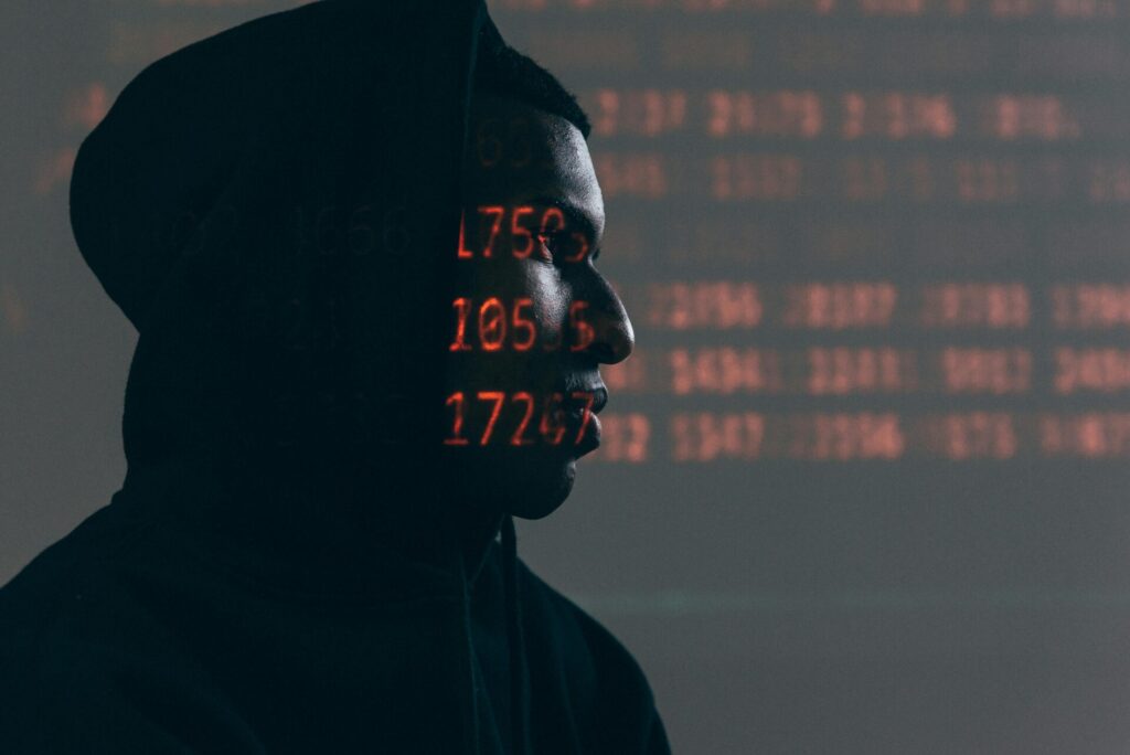Side profile of a man in a hoodie, surrounded by red code, depicting cybersecurity threats theme.